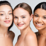 happy multiethnic women with bare shoulders isolated on grey